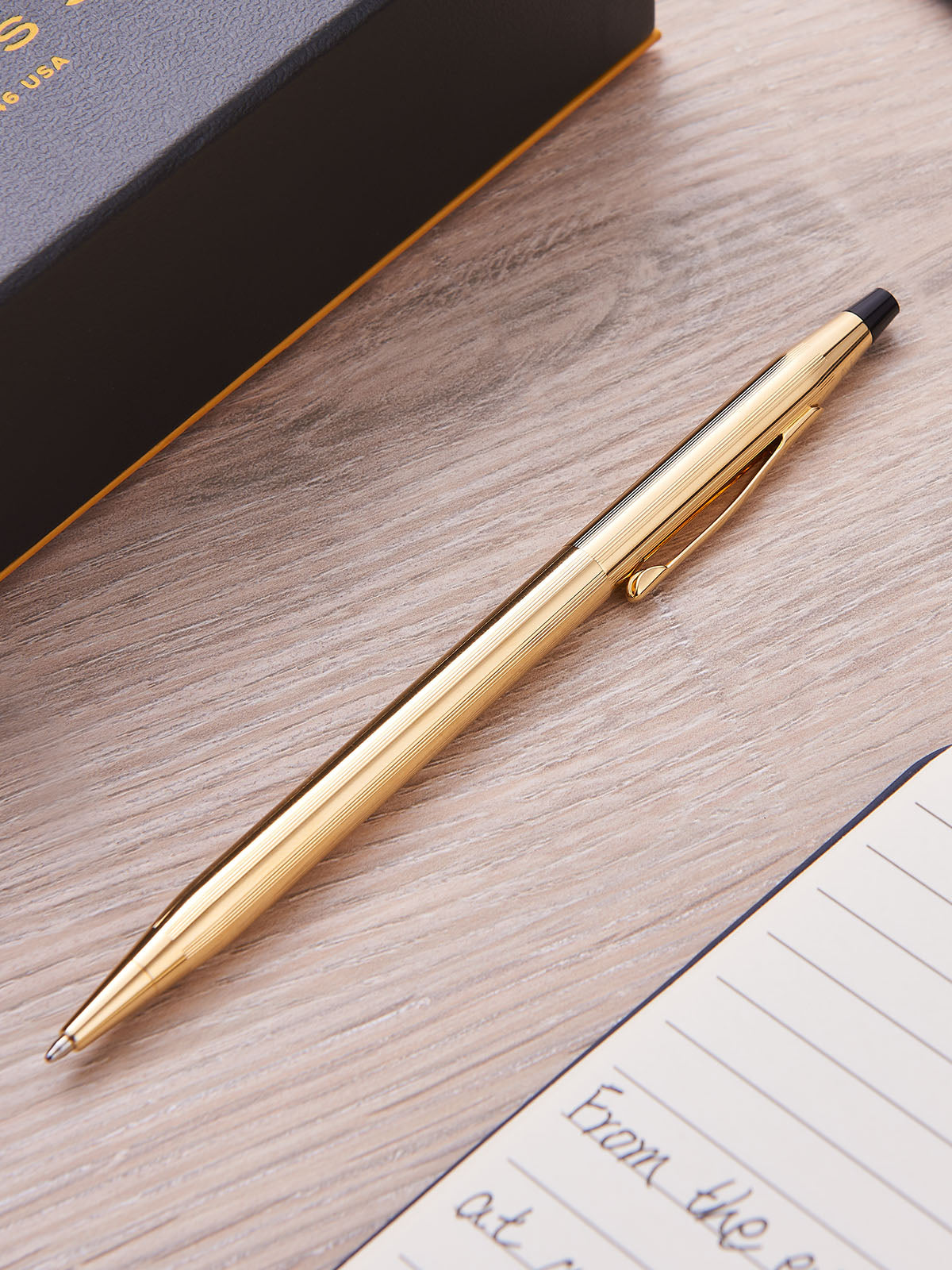 Gold-plated Cross Classic Century on a wooden surface with a notebookplated 